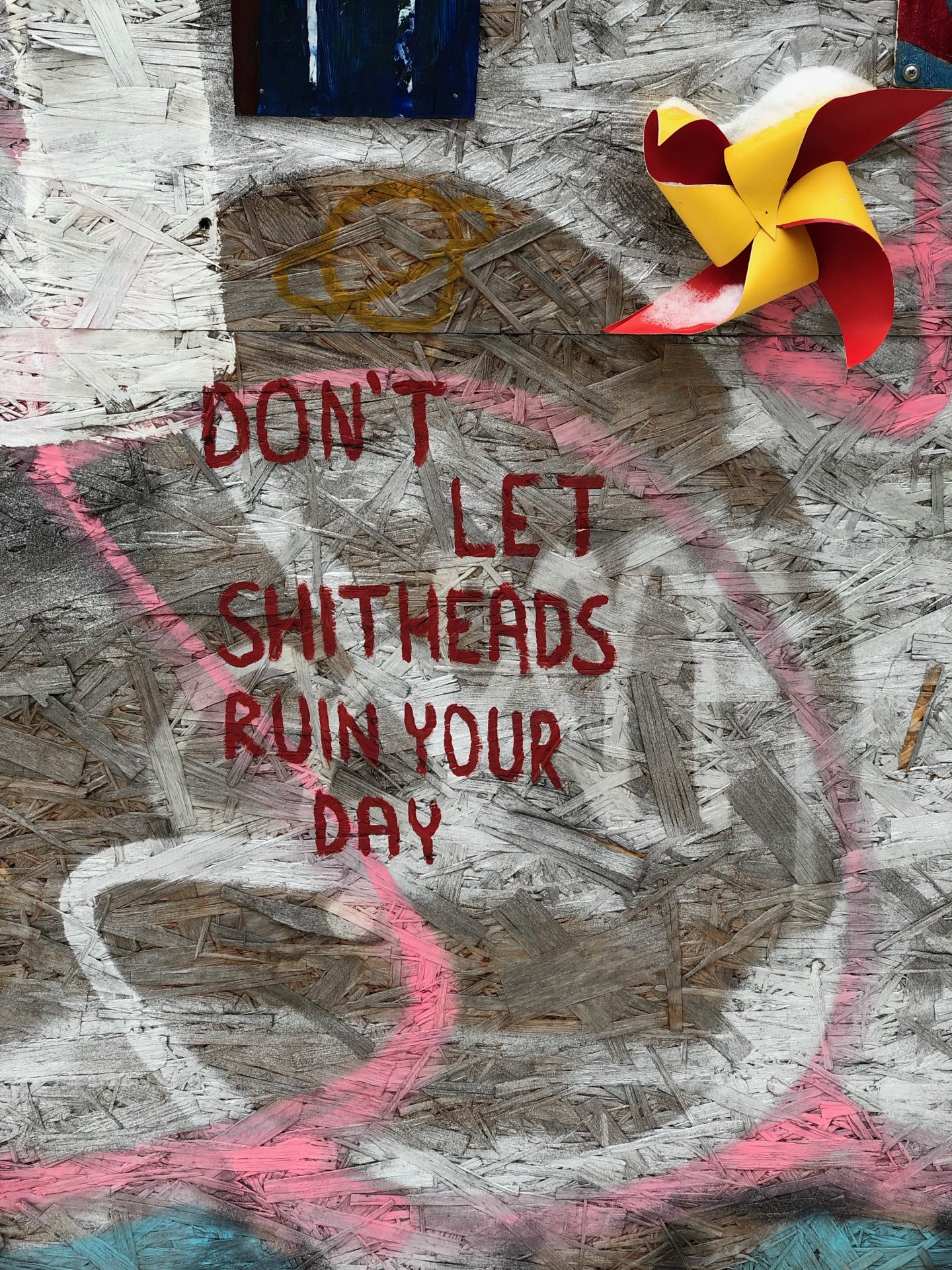 things to do in vilnius in winter: A wood-chip wall with the  words 'don't let the shit heads ruin your day' written in red writing. 