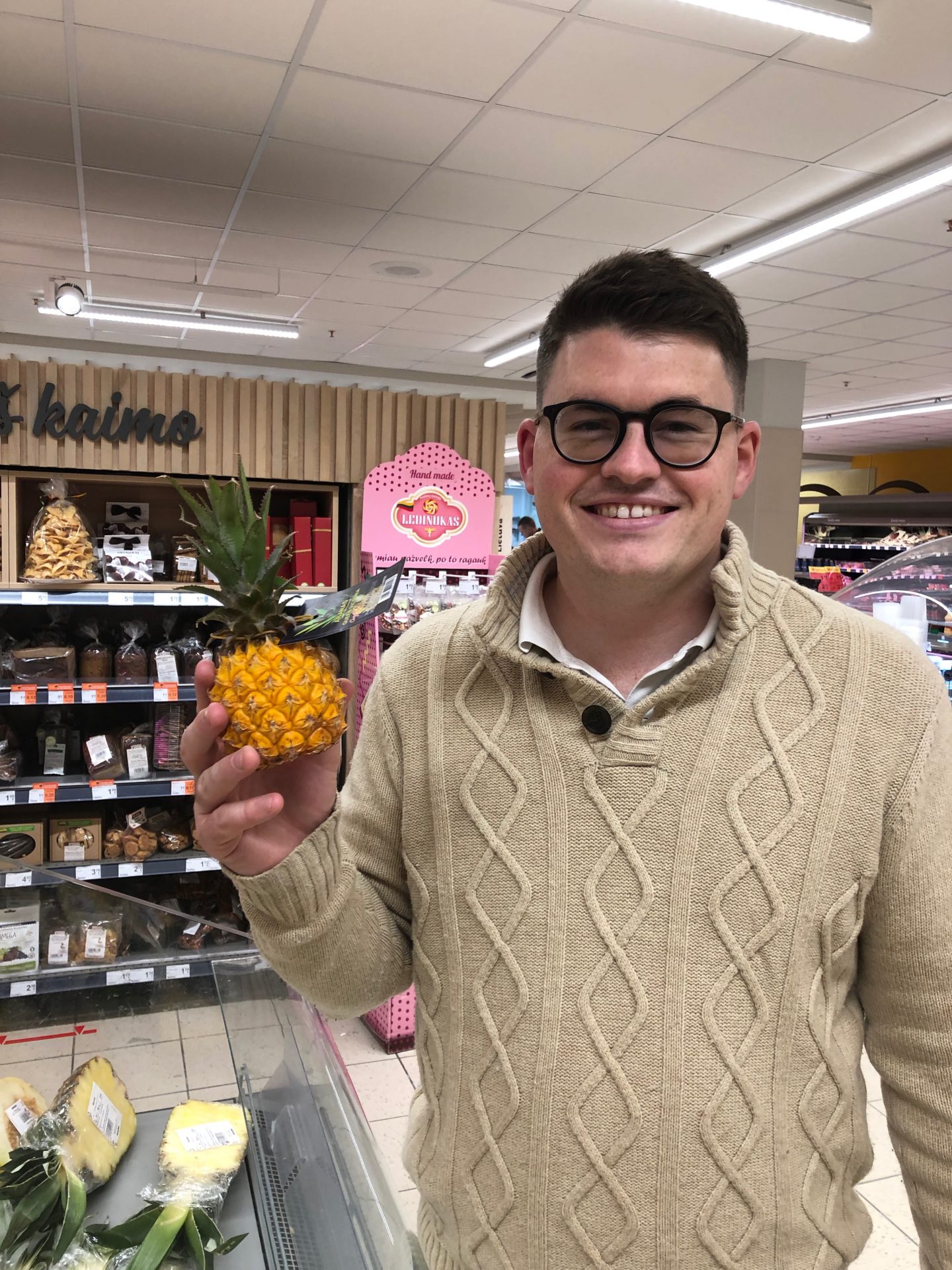things to do in Vilnius in winter: Billy in a supermarket in Vilnius holding a tiny pineapple and laughing