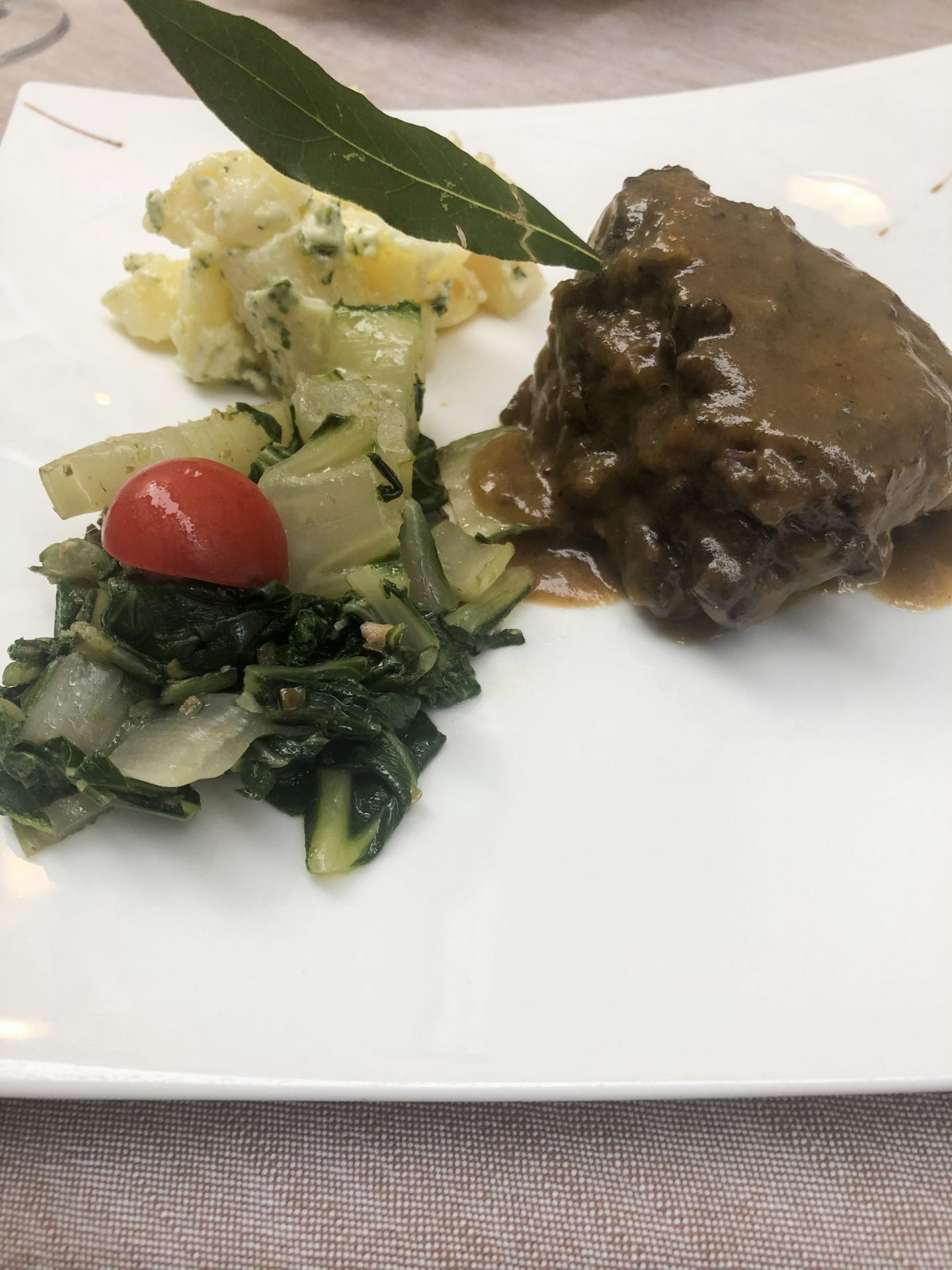 plate of calf cheek with potatoes and green vegetables in Trento, Trentino