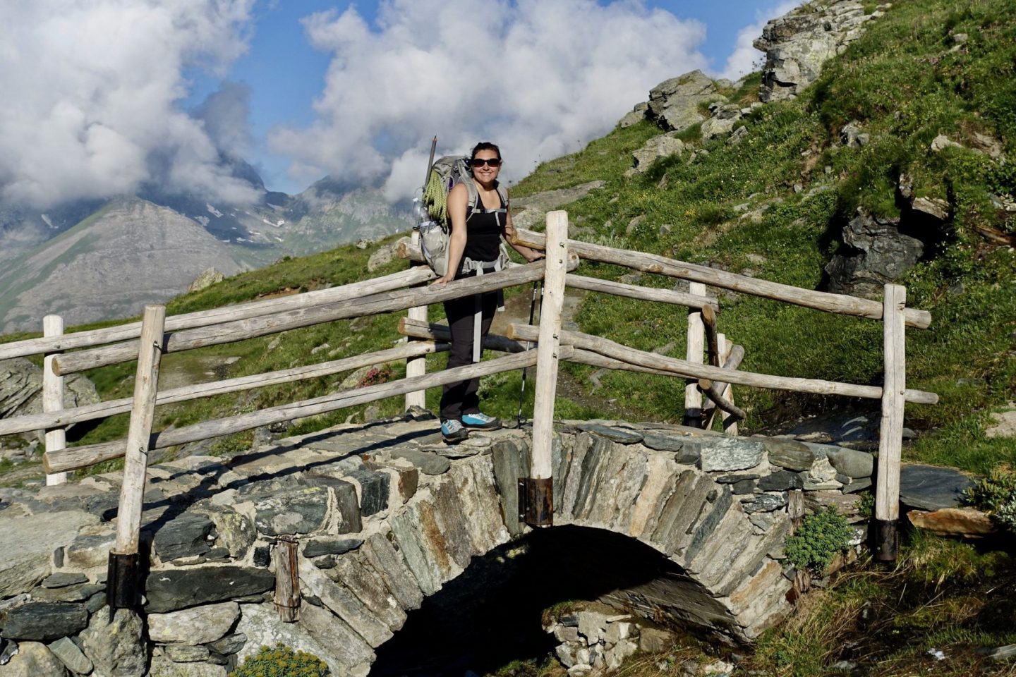 Nell on a bridge with mountains in the background wearing a back pack with ice axe and rope attached, on the spaghetti tour