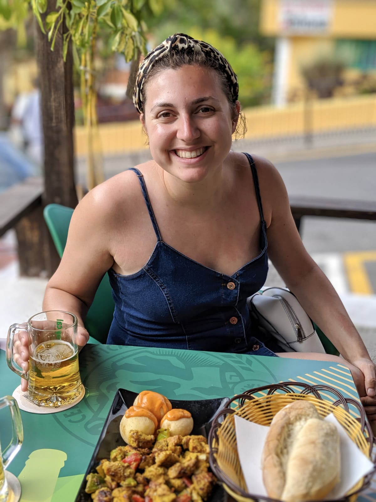 Girl looking into camera and smiling, with a beer and plate of potatoes in front of her. Taken in a roadside cafe in gran canaria.