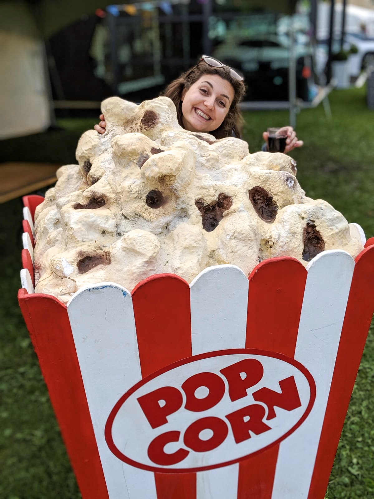 girl looking silly behind a giant box of popcorn with glass of red wine in her hand 