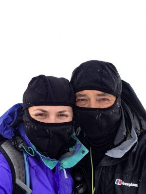 Father and daughter looking very cold at the top of Ben Nevis after walking the West Highland. They are looking directly into the camera but wearing balaclavas and snow is falling on them.