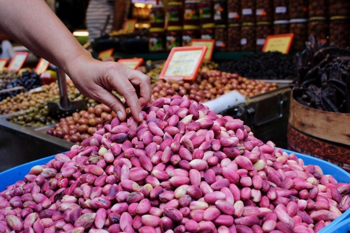 48 hours weekend in istanbul: A hand picking up a pink pistachio from a large pile of them in the spice market in Istanbul. In the background other buckets of nuts and olives are out of focus