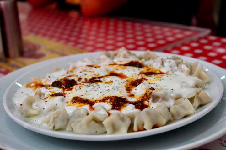 Turkish food in Istanbul: Manti dumplings in Istanbul. A close up of small dumplings with a sauce on top. served on a white plate with a red checked table cloth in the background.