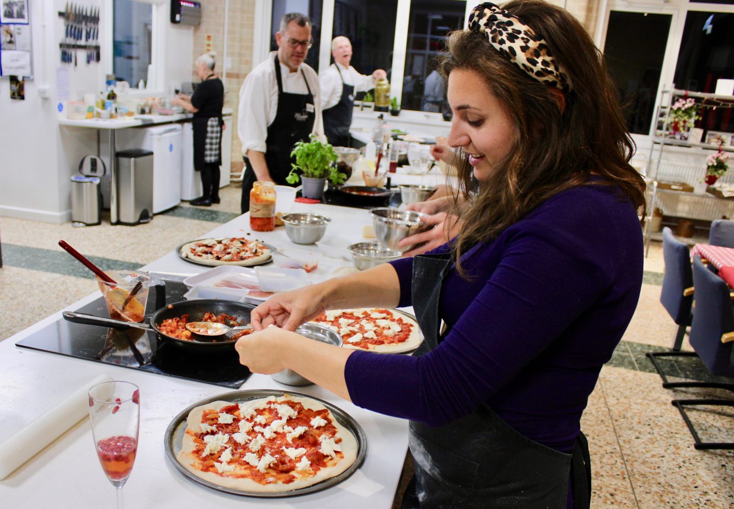 pizza making class leeds cookery school: Nell in blue dress with leopard print headband concentrating on topping her pizza during the pizza making class