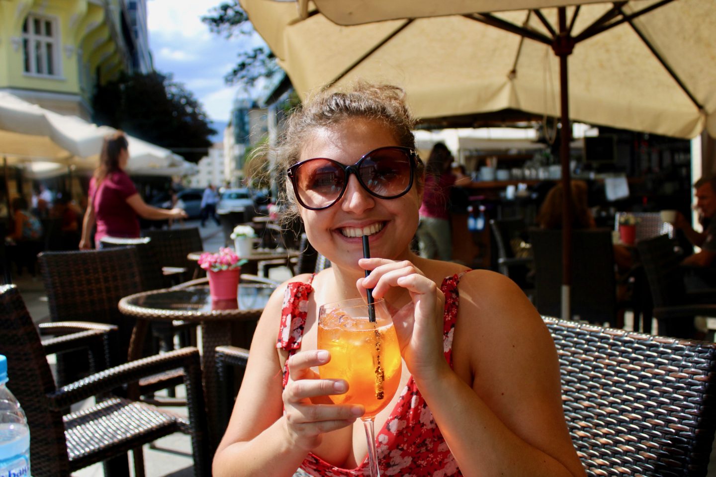 sofia city break: Nell in red floral dress wearing sunglasses and sipping an aperol spritz 