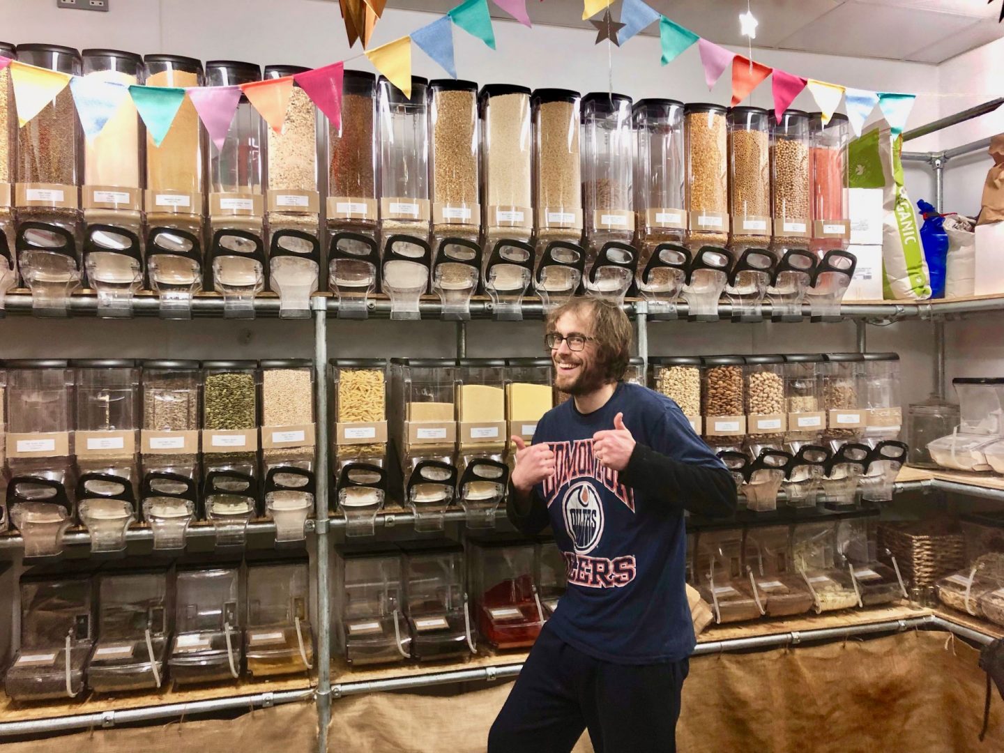 The inside of Jar Tree in Leeds Kirkgate Market showing products lined up in containers and the shop owner smiling and giving a thumbs up at the camera
