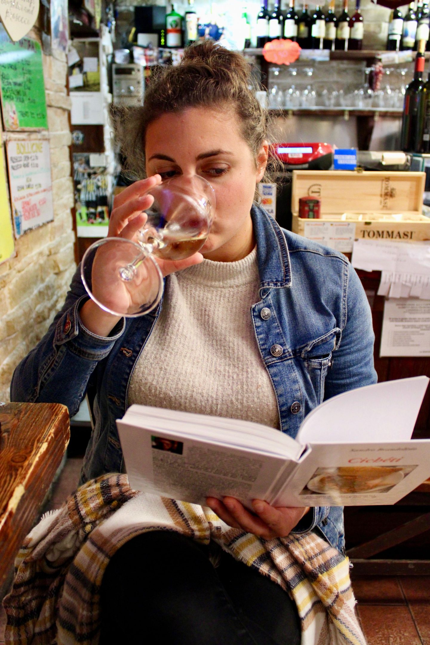 best cicchetti in Venice: Nell drinking a glass of white wine and reading a book about cicchetti