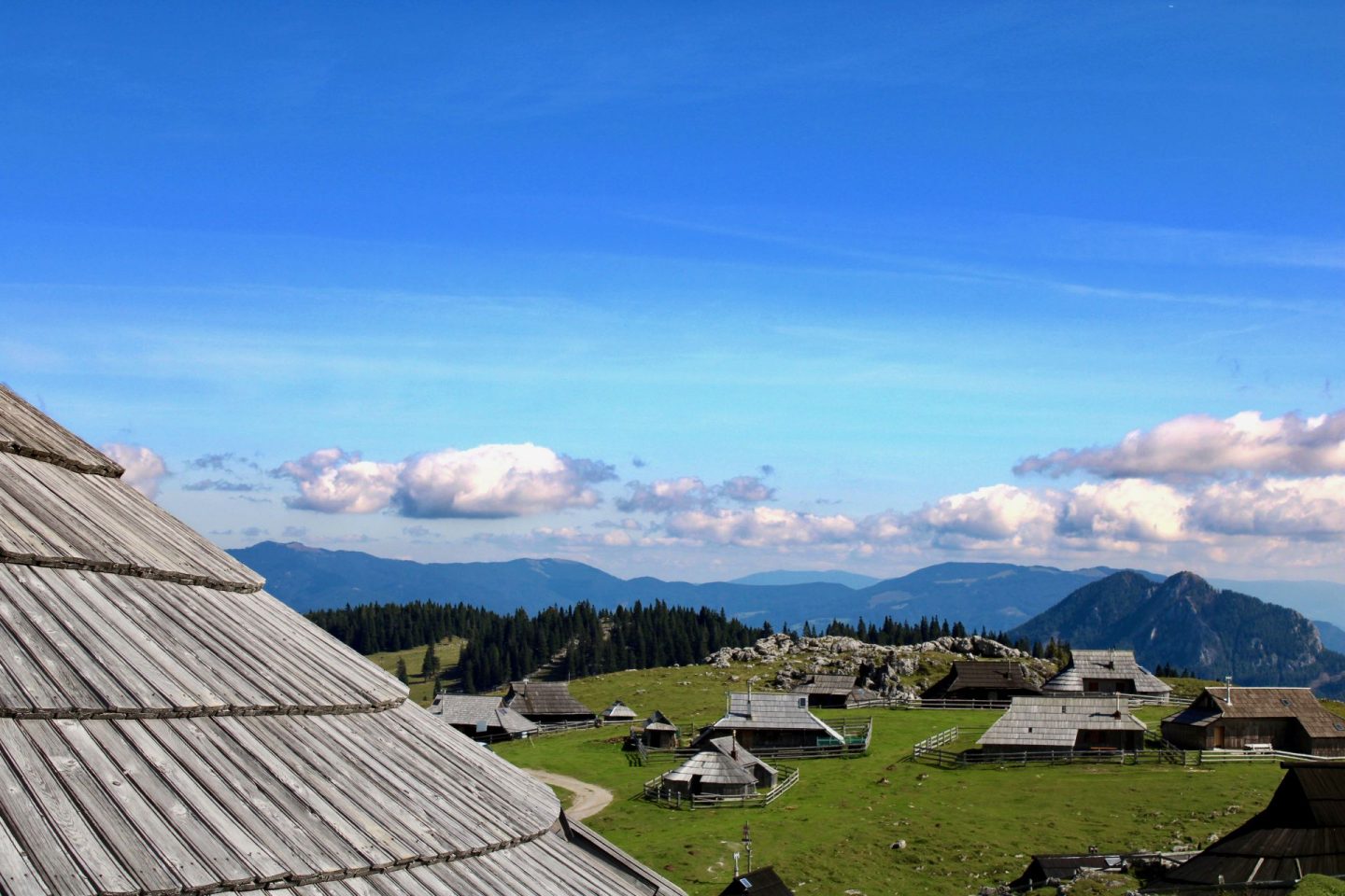 Valika Planina near Kamnik in the Ljubljana region. Image shows herdsman huts on green pasture with mountains in the background.