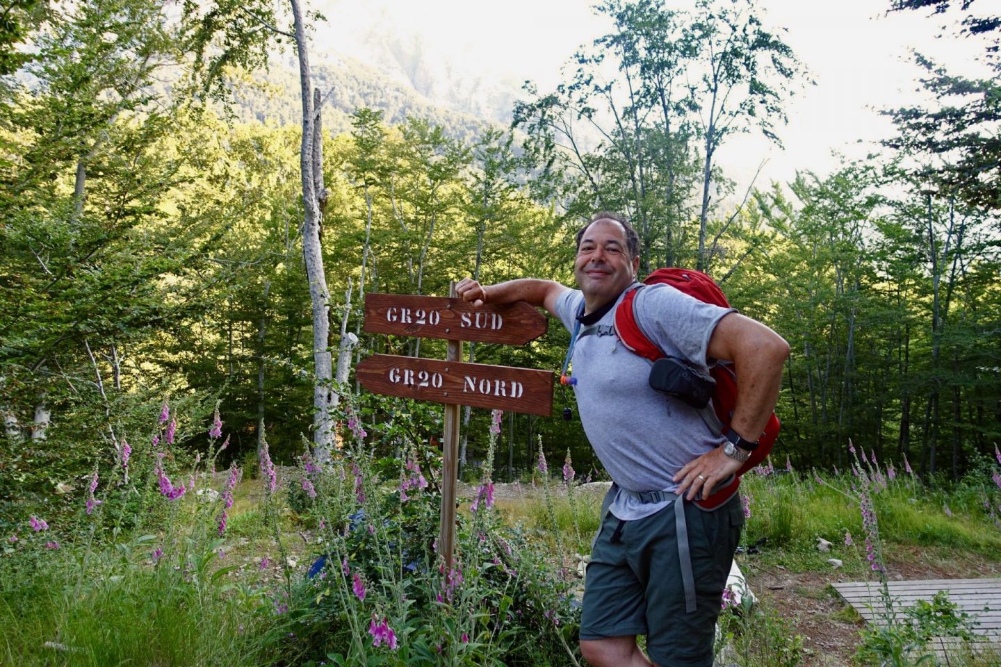 Nell's dad leaning against the half way sign, pointing to GR20 sud in one direction and GR20 Nord in the other. He's pulling a funny face and has one hand on his hip.