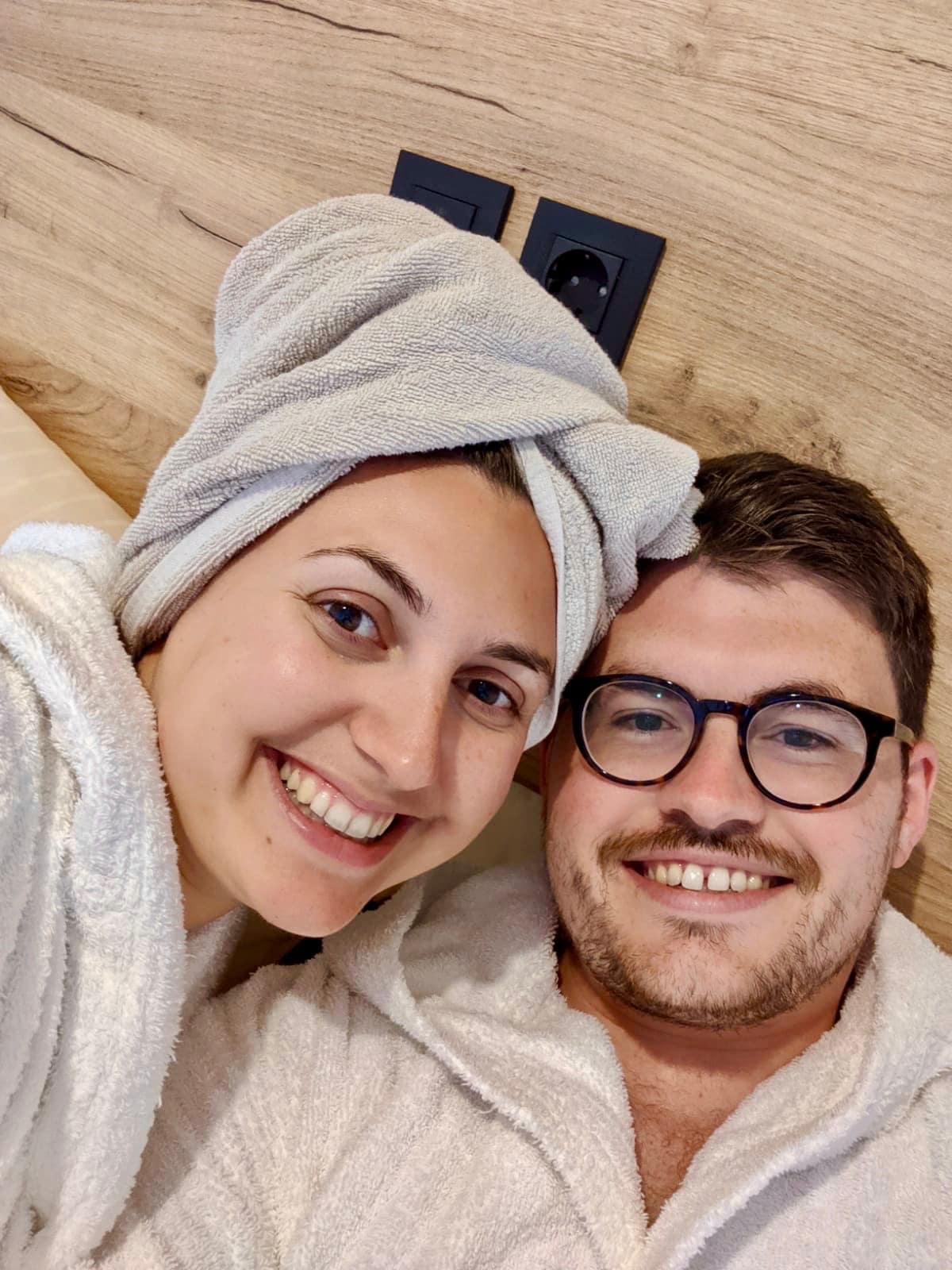Glamping in Slovenia: Selfie of couple wearing towel robes and smiling at the camera. The girl has a towel on her head and both look happy and relaxed
