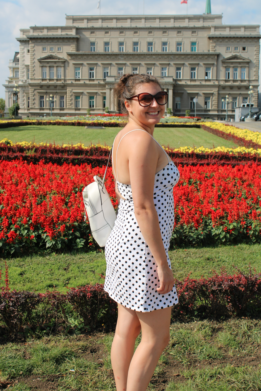 visit belgrade - Nell stood outside an official looking building with colourful flowers behind her 